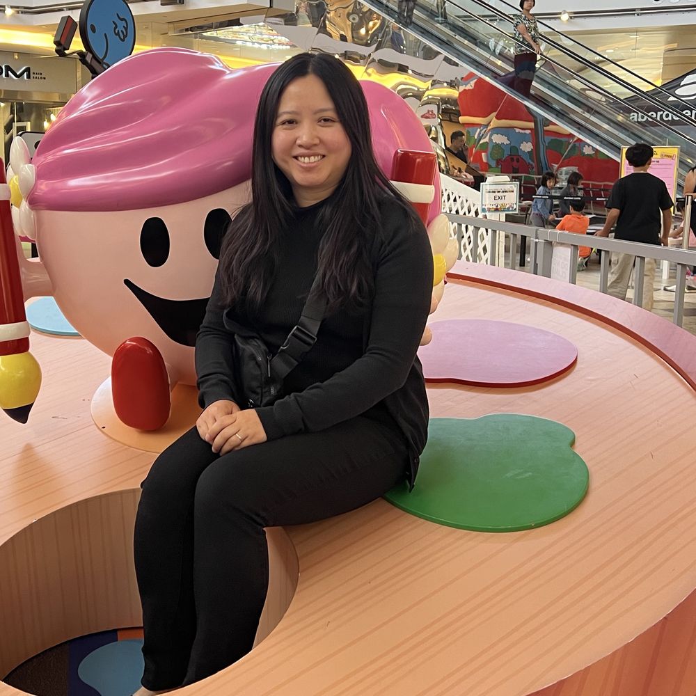 Janitta sitting on a giant toy palette beside a smiling cartoon character